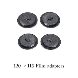 Peut inclure: Quatre adaptateurs de film noirs 120 à 116. Chaque adaptateur est rond avec un centre surélevé et un petit motif stylisé. Les adaptateurs sont disposés en carré sur fond blanc. Le texte "120 -> 116 Film adapters" est en dessous.