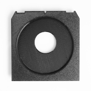 May include: A square, black, 3D-printed object with a circular indentation in the center. The object has a textured surface and a white background. The circular indentation has a white center.