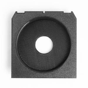 May include: A square, black, 3D-printed object with a circular indentation in the center. The center hole is white. The object has a textured surface and a small notch on the top edge.