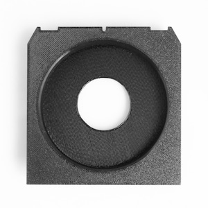 May include: A square, black, 3D-printed object with a circular opening in the center. The object has a textured surface and a smaller, white circular hole in the middle. The design features a raised rim around the central opening.