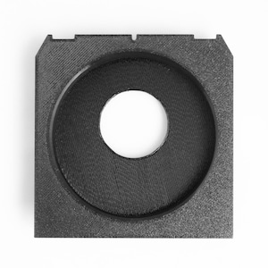 May include: A square, black, 3D-printed object with a circular opening in the center. The object has a textured surface and a raised rim around the central hole. The overall shape is geometric and industrial.