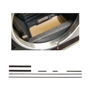 May include: A detailed view of a camera part, showing a silver metal frame and a black, textured foam strip. Inside, a light tan surface is visible. Beneath, there are several black foam strips of different lengths.