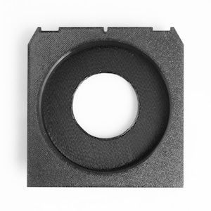 May include: A square, black, 3D-printed object with a circular opening in the center. The object has a textured surface and a raised, circular rim around the opening. The overall shape is geometric and modern.