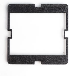 Könnte beinhalten: Ein schwarzer, rechteckiger Rahmen mit strukturierter Oberfläche und Ausschnitt. Der Rahmen hat eine quadratische Form mit Kerben an den Seiten und oben, vor weißem Hintergrund.