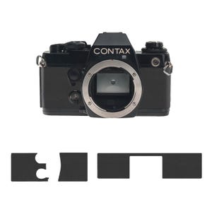 May include: A black Contax camera with a silver lens mount is displayed against a white background. The word "CONTAX" is printed in white on the camera body. Below the camera are four black, irregularly shaped pieces.