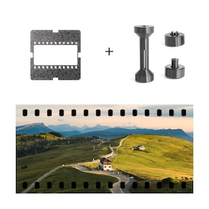 Puede incluir: Un portafilm negro y tres herramientas de procesamiento de película gris oscuro se muestran encima de una fotografía panorámica de una carretera de montaña. La fotografía muestra una carretera sinuosa a través de colinas verdes, con un edificio y montañas al fondo.