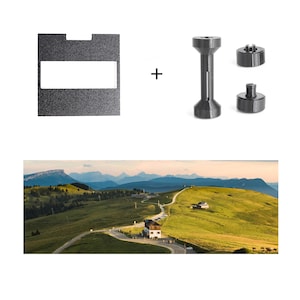 May include: A black textured square plate with a rectangular cutout, a black spool-shaped component, and two small black circular discs. Below these items is a landscape photograph showing a winding road through green hills and mountains.
