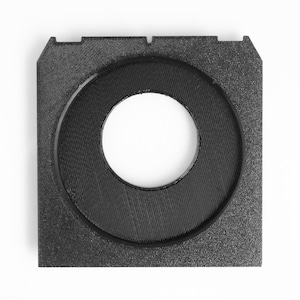May include: A square, black, 3D-printed object with a circular opening in the center. The object has a textured surface and a raised, circular rim around the opening. The corners of the square have small cutouts.