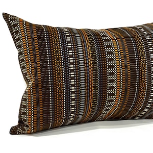 May include: A brown and orange striped lumbar pillow with a geometric pattern. The pillow is made of a woven fabric and has a subtle sheen.