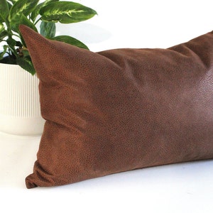 May include: A brown suede cushion with a textured surface.