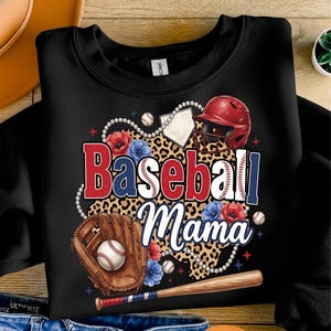 以下が含まれることがあります： 野球をテーマにしたデザインの黒いスウェットシャツ。デザインには、「Baseball Mama」の文字が赤、白、青で、野球ボール、グローブ、ヘルメット、バットとともに描かれています。フローラルアクセントとヒョウ柄の背景がデザインを完成させています。