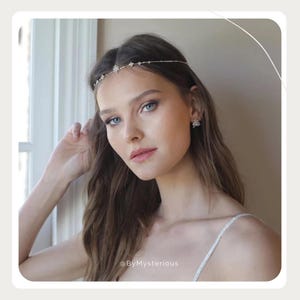 May include: A delicate silver-toned headband with small, sparkling embellishments. The headband is worn across the forehead. The model is also wearing matching earrings. The image is set against a soft background.