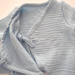 K&ouml;nnte beinhalten: Hellblaue Babyrobe aus weichem, strukturiertem Stoff. Die Robe hat ein Wickeldesign mit einem Bindeband in der Taille. Die &Auml;rmel sind kurz und die Kanten sind mit passendem Besatz versehen. Die Robe ist auf Komfort und einfache Handhabung ausgelegt.