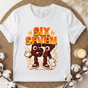 May include: White t-shirt with the words "SIX SEVEN" in orange and yellow, with a cartoon-like "6" and "7" character design. The characters have a cracked, lava-like texture and are wearing shoes and gloves.