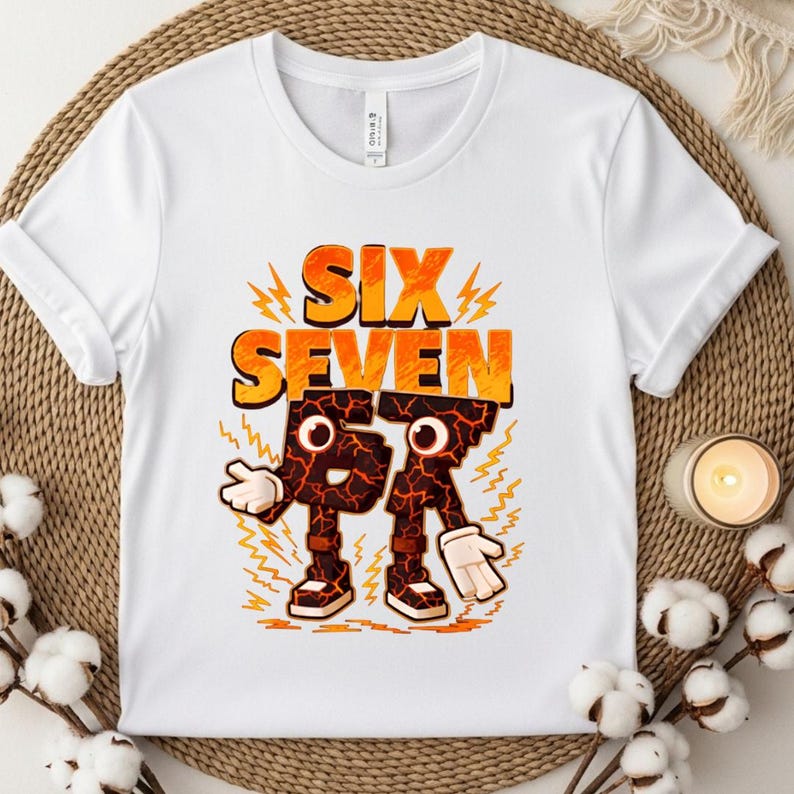 May include: White t-shirt with the words "SIX SEVEN" in orange and yellow, with a cartoon-like "6" and "7" character design. The characters have a cracked, lava-like texture and are wearing shoes and gloves.