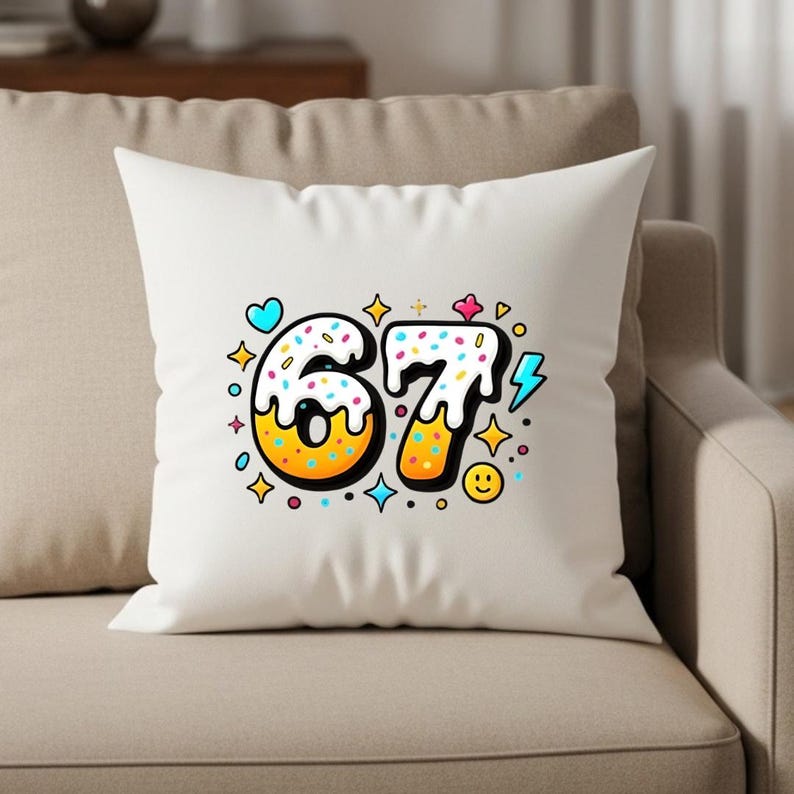 May include: White throw pillow with a colorful graphic of the number 67, designed to look like a donut with sprinkles. The design includes a blue heart, yellow stars, and a smiling face.