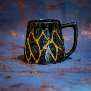 Könnte beinhalten: Schwarze Keramik-Tasse mit strukturierter Oberfläche und einzigartigem Design. Die Tasse weist ein Netzwerk aus gelb-orangen Linien auf, das einen auffälligen Kontrast erzeugt. Sie hat einen Henkel und ist für heiße oder kalte Getränke geeignet.