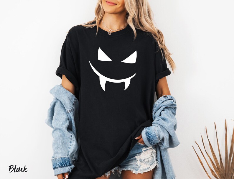 A woman wearing a black t-shirt with a white smiley face and a pair of denim shorts, standing against a white background.