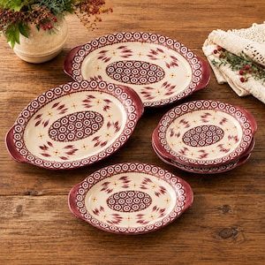 May include: A set of cream-colored ceramic serving dishes with handles, featuring a repeating maroon and yellow floral pattern and a central oval medallion with a circular geometric design. The collection includes two large oval platters and two round plates.
