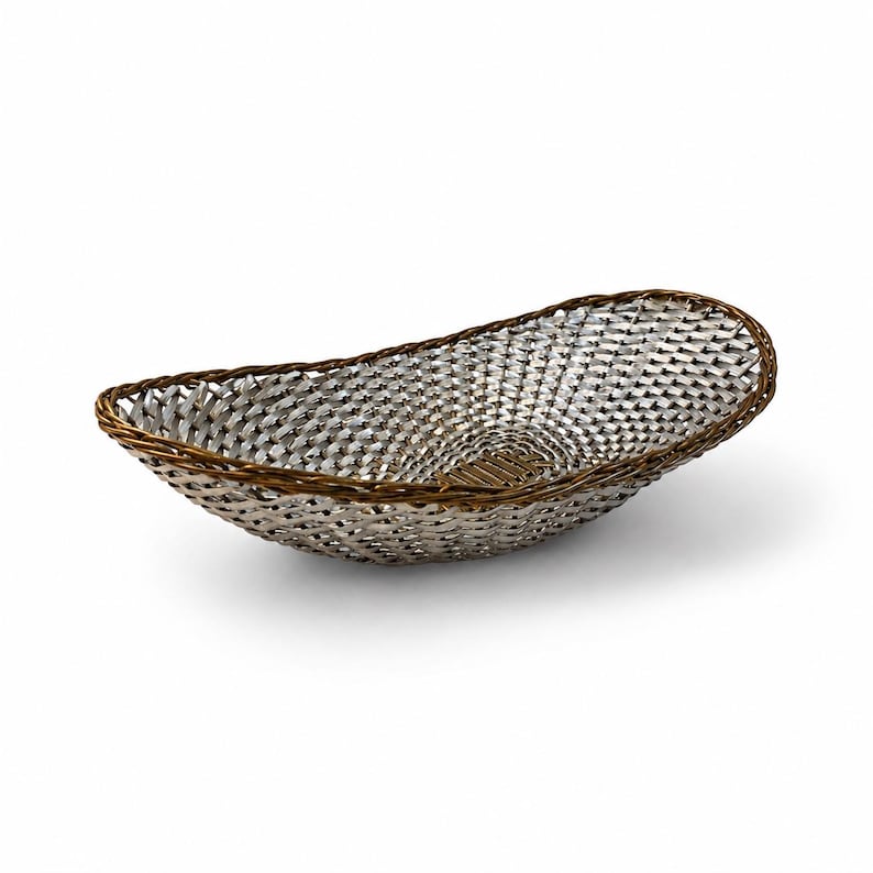 Puede incluir: Una cesta de forma ovalada con un cuerpo de metal plateado tejido con un patr&oacute;n de trama cruzada. El borde est&aacute; construido con un material trenzado de color marr&oacute;n oscuro que proporciona un contraste con el interior plateado reflectante.