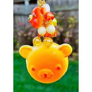 May include: A yellow bear charm with orange and white beads. The bear charm has a cute face with black eyes and a pink nose.