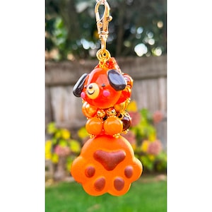 May include: Orange and brown beaded keychain with a dog charm and a paw print charm.