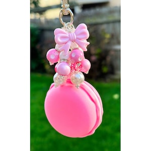 May include: Pink macaron charm with a pink bow and white and pink beads. The charm is attached to a silver chain.