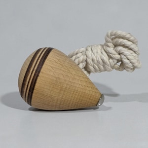 May include: A wooden spinning top with three dark brown stripes and a metal tip. A white rope is attached to the top. The top is made of light-coloured wood.