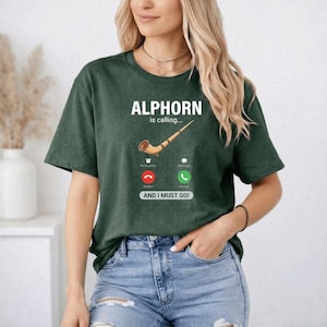 May include: Dark green t-shirt with the text "ALPHORN is calling..." and an illustration of an alphorn. The design includes a phone interface with "Decline" and "Accept" buttons, and the phrase "AND I MUST GO!"