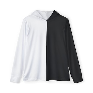 Puede incluir: Una sudadera con capucha de manga larga, dividida verticalmente en dos colores. Un lado es blanco y el otro negro. La sudadera tiene un diseño sencillo con capucha y puños. La prenda está hecha de una tela lisa, probablemente sintética.