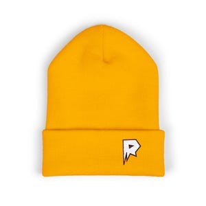 May include: Mustard yellow beanie with a folded brim. The beanie features a white and black embroidered logo on the front. The hat is made of a soft, knitted material.