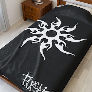 May include: Black and white duvet cover featuring a stylized sunburst design. The sunburst is white and has a tribal-inspired flame pattern. The word "FORSA" is printed in white at the bottom of the cover. The bedding is on a twin-sized bed.