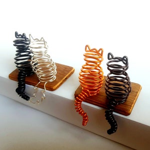 May include: Three wire-wrapped cat sculptures, each with a different coloured wire: black, silver, and orange. The cats are sitting on wooden bases.