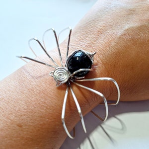 May include: A silver wire bracelet shaped like a spider with a black bead in the center.