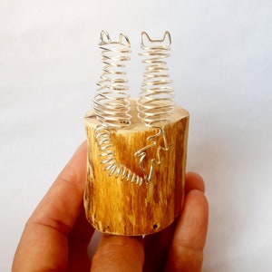 May include: Two silver wire sculptures of cats, standing on a wooden base. The cats are curled up in a playful pose.