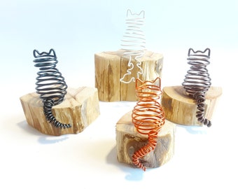 May include: Three wire cat sculptures in black, copper, and white, each sitting on a wooden log base.