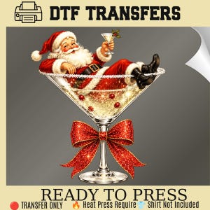May include: A DTF transfer graphic featuring Santa Claus wearing a red suit and white fur trim, reclining inside a large martini glass filled with a sparkling gold liquid and red berries. A large, glittery red bow is tied around the glass stem.