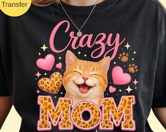 May include: Black t-shirt with a graphic featuring a smiling orange tabby cat, pink hearts, paw prints, and the words "Crazy MOM" in pink and leopard print. The shirt has a crew neck.