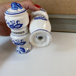 May include: White ceramic spice shakers with blue floral designs and the words "cinnamon" and "nutmeg". The shakers have a classic, vintage aesthetic, with a small handle on the lid.
