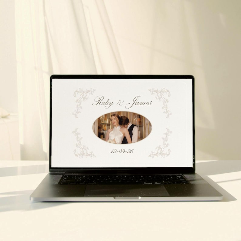 May include: A laptop displays a wedding photo album. The screen shows a photo of a couple in an oval frame, with the names "Ruby & James" above and the date "12-09-26" below. Floral designs frame the text.