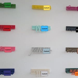 Peut inclure: Une collection de douze étagères murales de différentes couleurs, chacune présentant un mot ou une phrase en relief sur le devant. Les étagères sont disposées en grille et présentent des couleurs variées, notamment vert, jaune, rose, rouge, bleu clair, gris foncé, rose clair, argent, marron, bleu foncé, crème et sarcelle.
