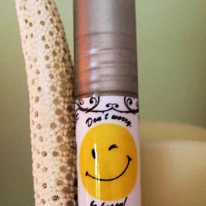 May include: A silver roller bottle with a white label featuring a yellow smiley face with a wink and the text "Don't worry, be happy!"