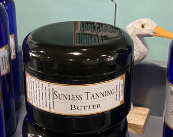 Może przedstawiać: Czarny słoik z białą etykietą, na której widnieje napis "SUNLESS TANNING BUTTER". Etykieta zawiera również tekst "Fragrance, Frankincense and Lavender Essential oils" oraz "Reorder by calling Occasional Treasures 724-854-1762".