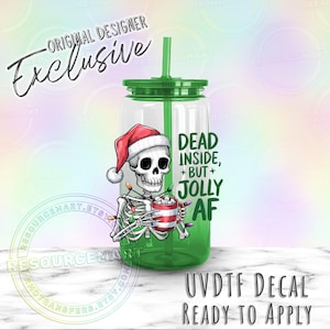 May include: A clear tumbler with a green lid and straw, featuring a skeleton wearing a Santa hat and holding a mug of marshmallows. The text reads "Dead Inside, But Jolly AF." The design includes Christmas lights and the words "Original Designer Exclusive."