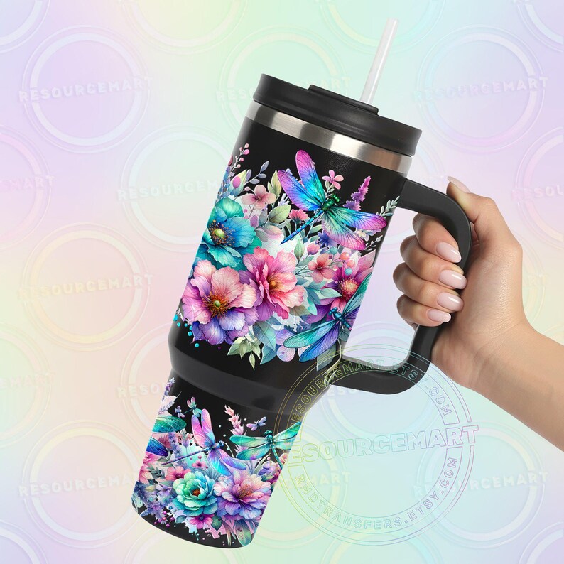 May include: Black tumbler with a floral and dragonfly design. The tumbler features a vibrant watercolor design of pink, purple, and blue flowers with teal and purple dragonflies. It has a black handle and a straw.