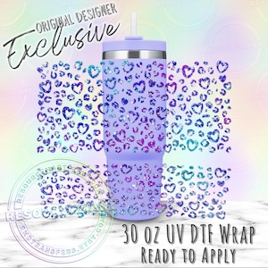 Puede incluir: Un vaso de color morado claro con pajita, con un patr&oacute;n repetitivo de corazones y manchas de leopardo brillantes en azul, morado y turquesa. El texto ORIGINAL DESIGNER Exclusive y 30 OZ UV DTF WRAP READY TO APPLY es visible.