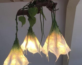 以下が含まれることがあります： 白と緑の繊維素材で作られた3つのベル型シェードを備えた吊り下げ式照明器具。シェードは、緑色の布製の葉と細い蔓のようなアクセントで飾られた、暗褐色の枝のような構造から吊り下げられています。