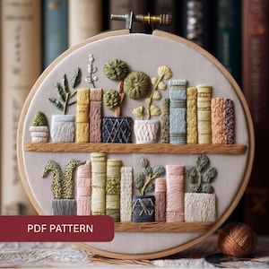 May include: Embroidered hoop art featuring a bookshelf design with books and potted plants. The artwork uses various colors, including green, pink, yellow, and blue. The text "PDF PATTERN" is displayed on a maroon banner at the bottom.