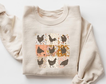 May include: Beige sweatshirt featuring a patchwork design of chickens and floral patterns. The design includes nine squares with brown chicken silhouettes on various floral backgrounds. The sweatshirt has a crew neck and long sleeves.