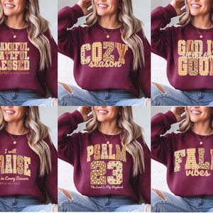 May include: Burgundy sweatshirts with various text designs in a mix of fonts and patterns. The designs include phrases like "Thankful, Grateful, Blessed", "Cozy Season", "God is all the time Good", "I will Praise", "Psalm 23", and "Fall Vibes".